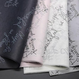 Puede incluir: Cuatro hojas de papel de seda en negro, rosa claro y blanco, cada una con un patrón repetitivo en letra cursiva que dice "Flowers be beautiful as flowers" y "Beauty to your life" en tintas de colores contrastantes sobre las superficies.