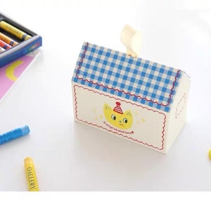 May include: A white house-shaped gift box with a blue and white checkered roof. The box has a yellow cat with a red party hat on the front and the text "Congratulations!" printed below the cat.