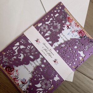 May include: Purple laser cut wedding invitation with a floral design and gold glitter accents. The invitation includes the names Sherminch Deimaran & Wader Maghavi and the date 7th July 2020.