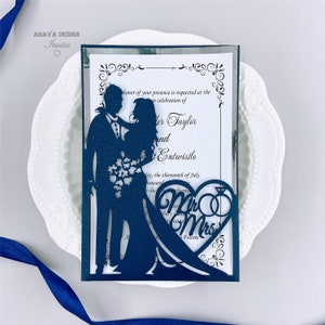 May include: Navy blue laser cut wedding invitation with a silver glitter background. The invitation features a silhouette of a couple holding a bouquet of flowers. The text on the invitation reads "In honour of your presence is requested at the celebration of [Name] Taylor and [Name] Entwistle, May, the thirteenth of July, two thousand [Year] at [Time] o'clock.  Mr. & Mrs. Follow."
