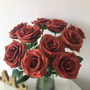 Puede incluir: Un ramo de rosas marrones artificiales en un jarrón de vidrio transparente. Las rosas están dispuestas en forma circular y tienen una textura aterciopelada.