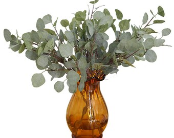 May include: A bouquet of artificial eucalyptus sprigs in a brown glass vase with a ruffled top.