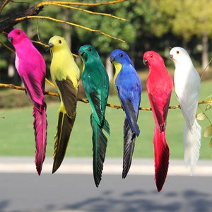 Könnte beinhalten: Sechs bunte künstliche Vögel mit langen Schwänzen, die auf einem Ast sitzen. Die Vögel sind rosa, gelb, grün, blau, rot und weiß.