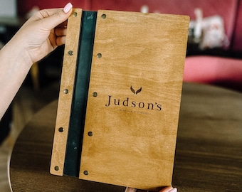 May include: A wooden menu with a black spine and metal rivets. The menu is open and the text "Judson's Wine Bar & Dining" is visible.