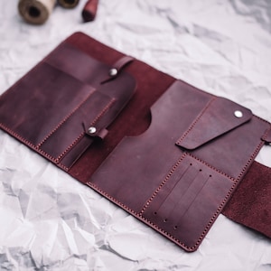 May include: A burgundy leather wallet with multiple compartments and pockets, open to reveal the interior.