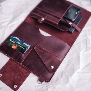 May include: A burgundy leather portfolio with multiple pockets and slots for cards, a phone, and other items. The portfolio is open and the interior is visible.