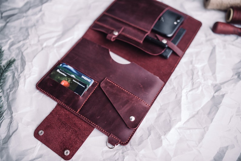 May include: A burgundy leather portfolio with multiple pockets and slots for cards, a phone, and other items. The portfolio is open and the interior is visible.