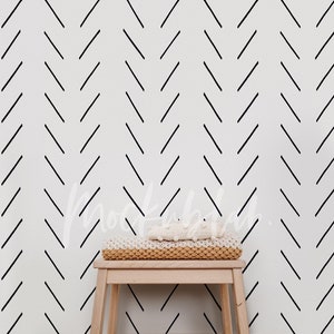 May include: A white wall with a black chevron pattern. A wooden stool with a white knitted blanket on top sits in front of the wall.