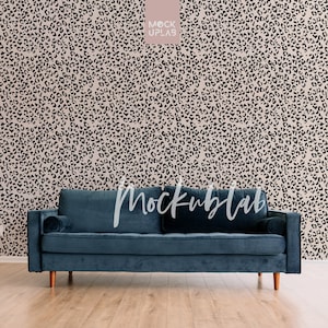 May include: A dark blue velvet sofa with two pillows sits in front of a wall with a black and beige leopard print wallpaper. The sofa has wooden legs.