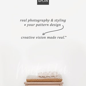 May include: A white wall with the text "MOCK UPLAB" in black. Below the text is the phrase "real photography & styling + your pattern design" in black. An arrow points to the text "creative vision made real." A wooden stool with a white and beige knitted blanket on top.