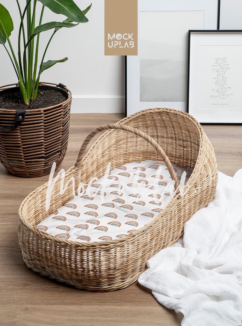 K&ouml;nnte beinhalten: Ein Weidenkorb-Babybett mit einem wei&szlig;en Laken und einem Regenbogenmuster. Das Babybett steht auf einem Holzboden mit einer wei&szlig;en Decke und einer Topfpflanze im Hintergrund.