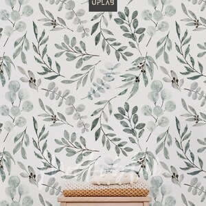 May include: A white wall with a green watercolor leaf pattern. A small wooden stool with a knitted blanket on top sits in front of the wall.