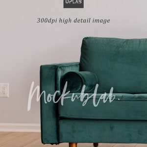 May include: A dark green velvet sofa with a matching pillow. The sofa has wooden legs and is sitting on a light wood floor.