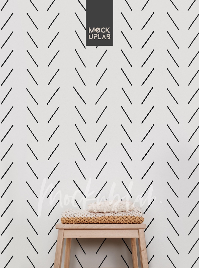 May include: A white wall with a black chevron pattern. A wooden stool with a white knitted blanket on top sits in front of the wall.