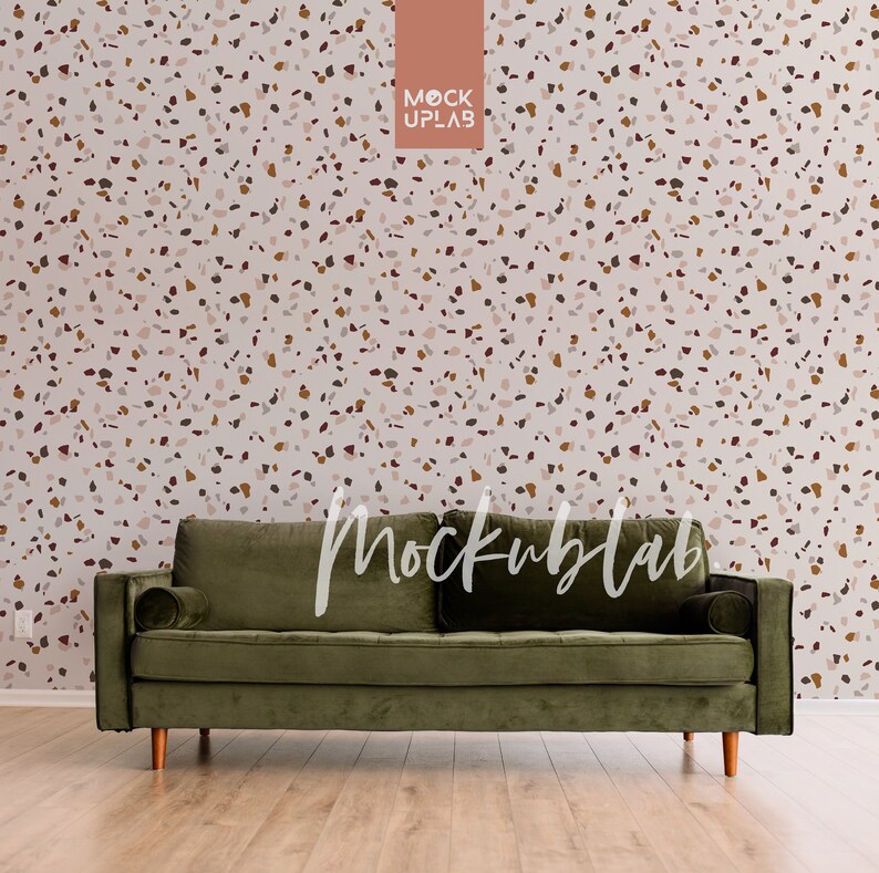 May include: A dark green velvet sofa with wooden legs sits in front of a wall with a terrazzo pattern. The wall is a light beige color with brown, red, and white flecks.
