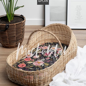 K&ouml;nnte beinhalten: Ein Weidenkorb-Babybett mit einer floralen Innenausstattung. Das Babybett steht auf einem Holzboden mit einer wei&szlig;en Decke in der N&auml;he.