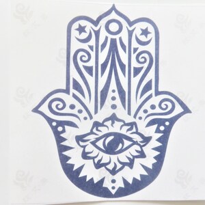 Può includere: Una mano di hamsa blu e bianca con un occhio al centro. La hamsa è un simbolo di protezione e buona fortuna.