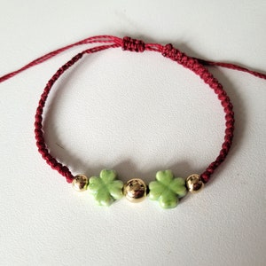 May include: A red string bracelet with three green four-leaf clover charms and gold beads.