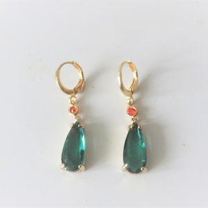 May include: A pair of gold hoop earrings with a teardrop-shaped green gemstone and a small orange gemstone hanging from each hoop.