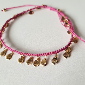 Peut inclure: Bracelet en macramé rose avec des breloques coquillages dorées. Le bracelet réglable présente un design tissé avec de petits pendentifs coquillages suspendus. Le bracelet est de couleur rose vif et comporte des perles dorées aux extrémités.