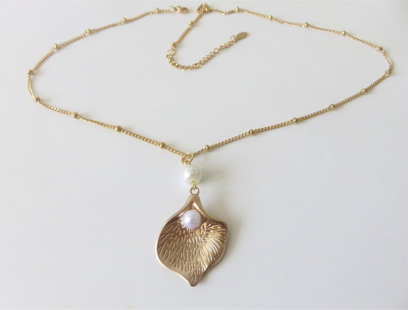 May include: A gold chain necklace with a delicate gold leaf pendant featuring a white pearl in the center. The chain is made of small gold beads.