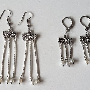 May include: A pair of silver dangle earrings with three chains and pearl accents. The earrings have a decorative, ornate design at the top.
