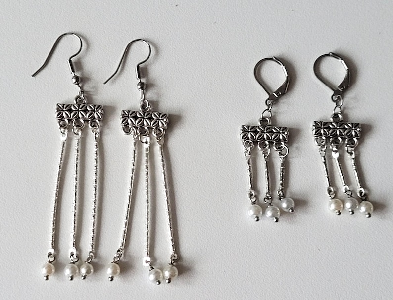 May include: A pair of silver dangle earrings with three chains and pearl accents. The earrings have a decorative, ornate design at the top.