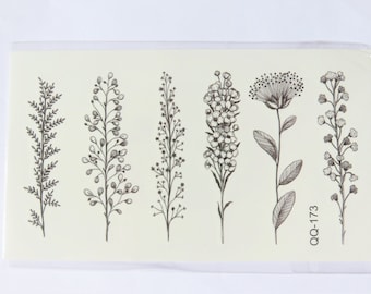 Puede incluir: Una hoja de tatuajes temporales con seis diseños florales en blanco y negro. Los diseños incluyen varios tipos de flores y hojas. La hoja está etiquetada como "QQ-173".