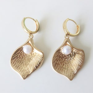 May include: A pair of gold hoop earrings with a textured petal-shaped charm and a white pearl accent.