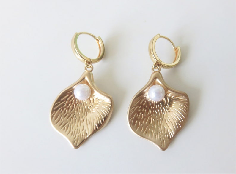 May include: A pair of gold hoop earrings with a textured petal-shaped charm and a white pearl accent.