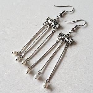 May include: Silver dangle earrings with a cluster of flower charms and pearl accents.