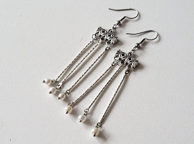 May include: Silver dangle earrings with a cluster of flower charms and pearl accents.