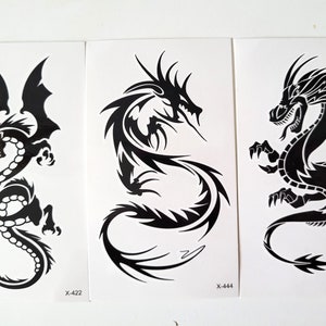 Può includere: Tre fogli di tatuaggi temporanei con disegni di draghi neri. Ogni drago è raffigurato in una posa diversa, con dettagli intricati e uno stile grafico audace. I fogli sono etichettati con i codici X-422, X-444 e X-431.