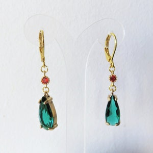 May include: A pair of gold dangle earrings with a teardrop-shaped green gemstone and a small red gemstone accent.