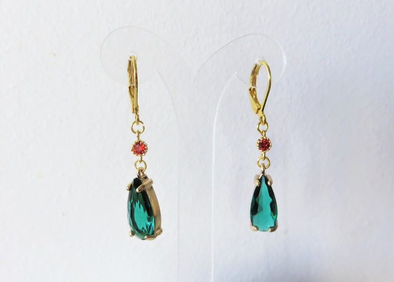 May include: A pair of gold dangle earrings with a teardrop-shaped green gemstone and a small red gemstone accent.