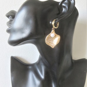 May include: Gold hoop earrings with a dangling gold leaf charm and a white pearl accent.