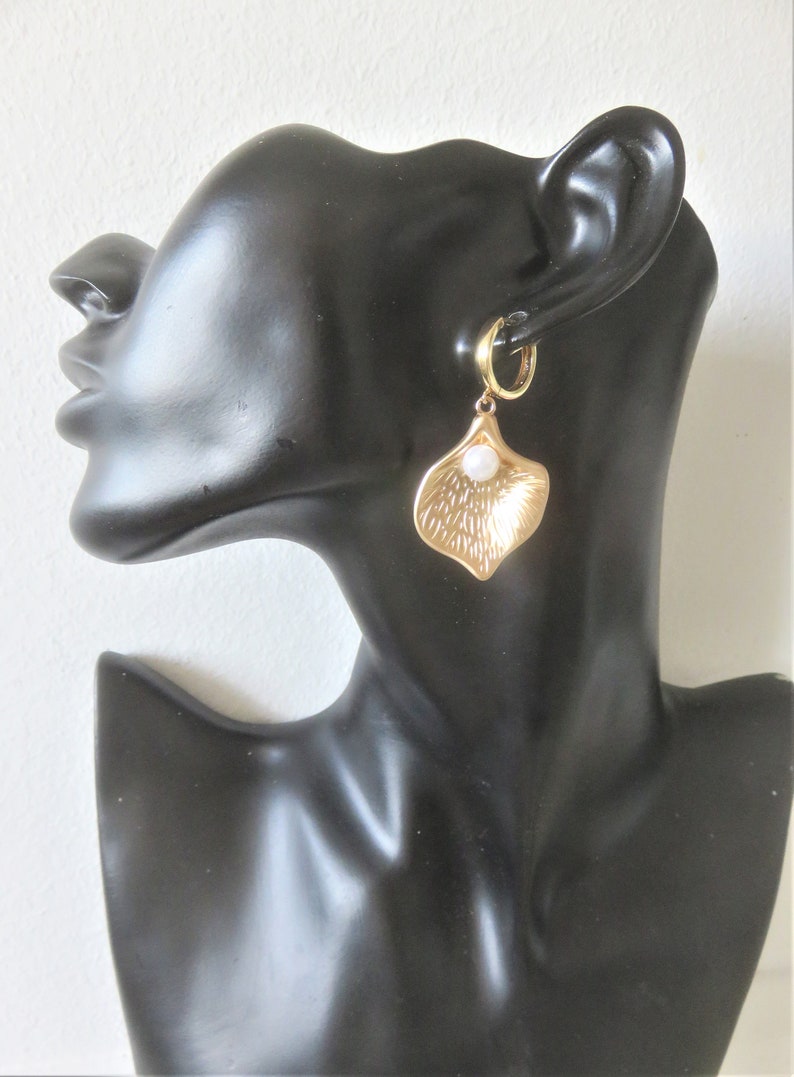 May include: Gold hoop earrings with a dangling gold leaf charm and a white pearl accent.