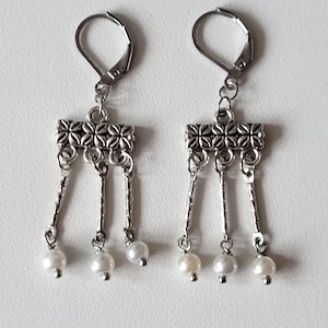 May include: Silver dangle earrings with a decorative silver bar and three white pearl drops.