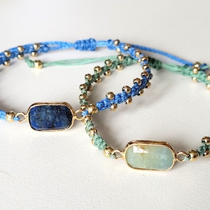 May include: Two bracelets with blue and green cords and gold beads. One bracelet has a rectangular lapis lazuli stone, the other has a rectangular aquamarine stone.