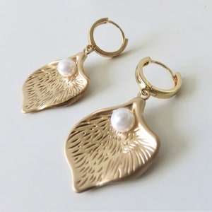 May include: Gold hoop earrings with a textured leaf-shaped pendant and a white pearl accent.