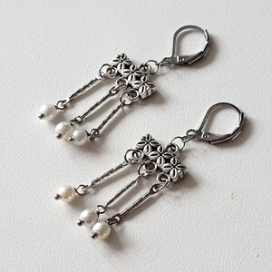 May include: A pair of silver dangle earrings with a floral design and white pearl accents.