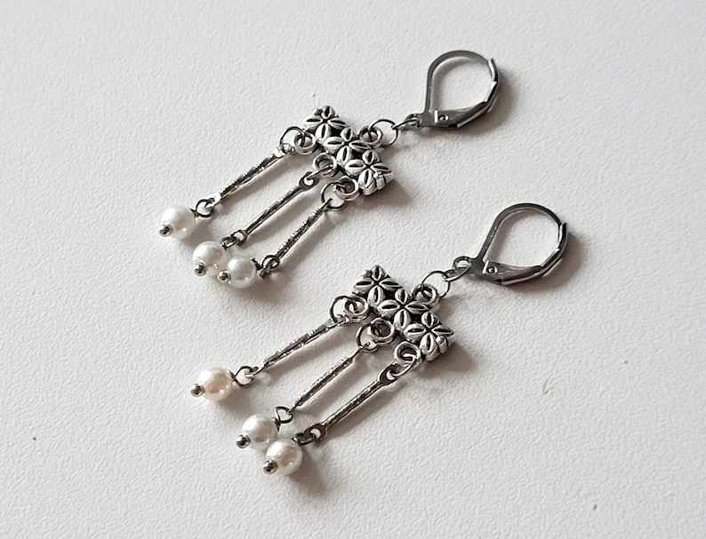 May include: A pair of silver dangle earrings with a floral design and white pearl accents.