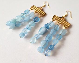 May include: Gold dangle earrings with a geometric design and multiple strands of light blue gemstone beads.