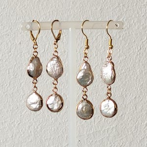 May include: A pair of gold dangle earrings with two white pearl drops on each earring.