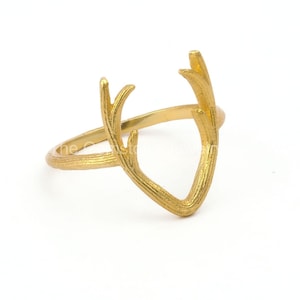 May include: A gold-colored ring with an antler design. The ring features a textured band and a stylized antler shape, creating a nature-inspired accessory. The ring is set against a white background.