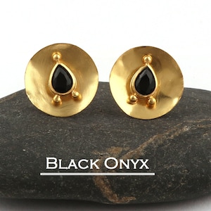 Puede incluir: Un par de pendientes dorados con una piedra negra en forma de lágrima de ónix en el centro. Los pendientes tienen un diseño circular con tres pequeños detalles dorados debajo del ónix. El texto "BLACK ONYX" se muestra debajo.