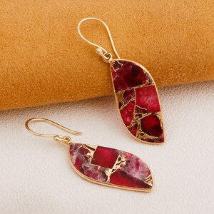 Puede incluir: Un par de pendientes dorados con forma de hoja. Los pendientes presentan un mosaico de piedras de color rojo intenso y dorado, engastadas en un marco dorado. Los pendientes tienen un cierre de gancho.
