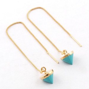 Può includere: Un paio di orecchini a filo dorati con pendenti turchesi a forma di piramide. I pendenti hanno un bordo dorato. Gli orecchini sono esposti su sfondo bianco.