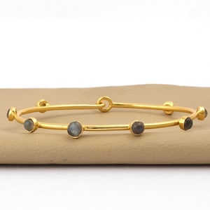 May include: A gold bangle bracelet with six round labradorite gemstones. The bracelet is open and has a hinge closure.