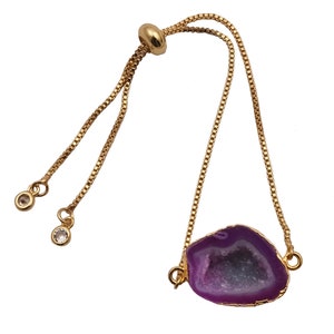May include: A gold chain bracelet with a purple agate stone pendant. The pendant is a geode with a crystal-like interior. The bracelet has an adjustable clasp.